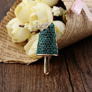 Macro shot of gold popsicle brooch with dark green and clear rhinestones on wood