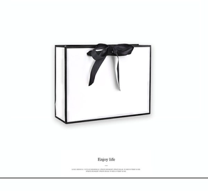 Close-up of elegant white gift bag with black ribbon bow and Enjoy Life text detail
