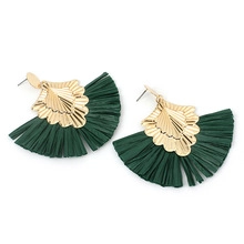 Détail de boucles d'oreilles à pompons en raphia vert avec clous en métal doré en éventail