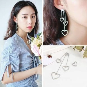 Detailed views of asymmetrical silver heart tassel earrings worn by a female model