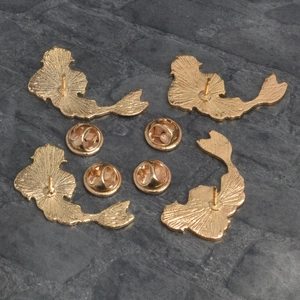 Golden mermaid enamel pin backs with butterfly clutch fasteners on dark stone