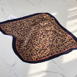Detailed view of a stylish pleated leopard print square scarf with dark blue borders on marble.