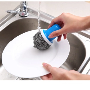 Blue handle wire scrub brush cleaning a white ceramic plate in a kitchen sink