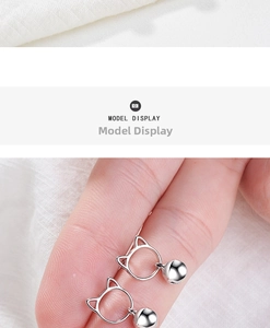 Detailed view of silver cat head earrings with bell charms held on a finger