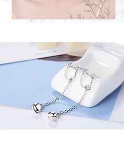 Close-up of S925 silver cat earrings with bells and long chains on white ceramic
