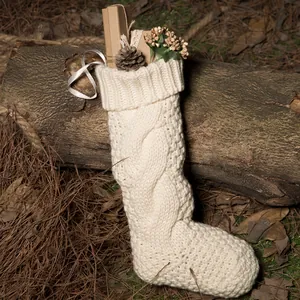 White cable knit Christmas stocking with festive pine cones and gift box on wood