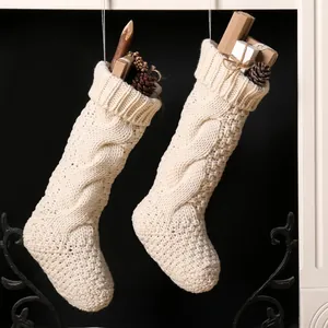 Set of two cream cable knit Christmas stockings with pine cones and gift box decor