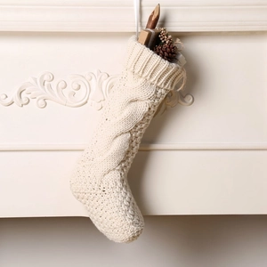 Detail of cream cable knit Christmas stocking with festive decor hanging on a mantel