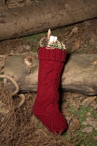 Close-up of red cable knit Christmas stocking with pine cones and gift box decor