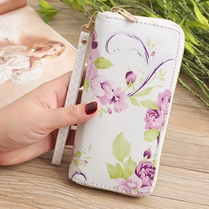Detail der weißen Geldbörse mit lila Blumenmuster und geflochtener Handschlaufe
