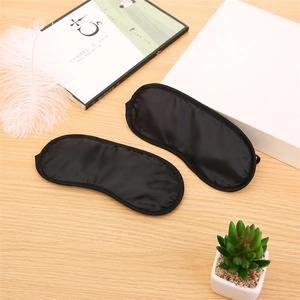 Two black silk sleep masks on a cozy desktop with feathers and a small green plant
