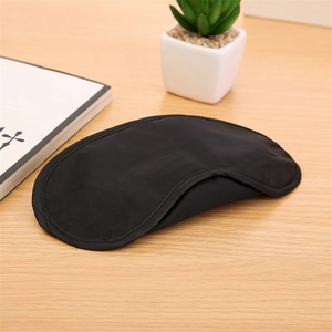 Detail of a breathable black sleep mask on a wooden desk with a green succulent plant