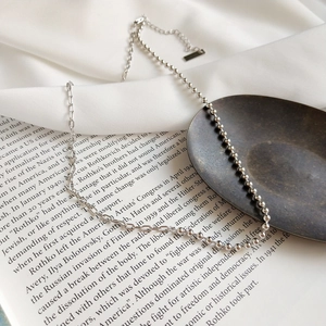 Artistic detail of silver-toned asymmetrical bead and link chain necklace on book
