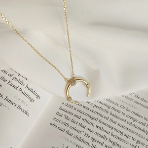 Detail of gold crescent moon necklace with zircon stones on white silk and book