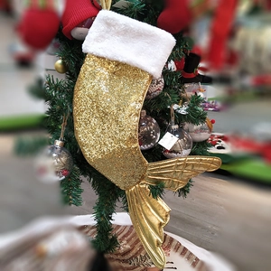 Golden sequin mermaid tail Christmas stocking with plush trim hanging on a festive tree