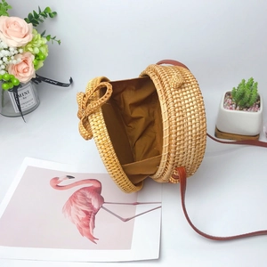 Handmade round rattan crossbody bag with brown lining and leather strap on white background