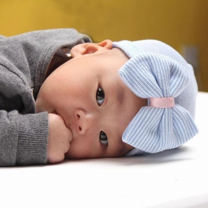 Close-up of a blue striped baby hat with a large bow and pink ribbon center detail