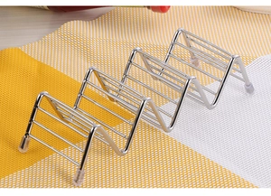 Detail of wavy stainless steel taco holder with non-slip feet on a woven kitchen mat