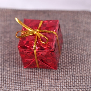 Close-up of a small red glitter gift box with gold ribbon on dark grey burlap surface