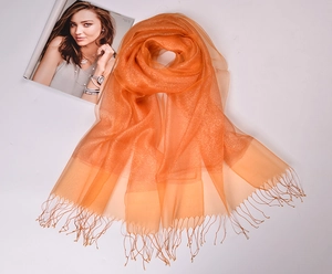 Detail of orange silk organza scarf with gold glitter and fringe tassels over a magazine