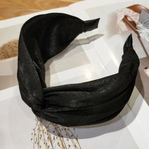 Detailed view of black satin fabric texture and cross-knot design on a wide headband