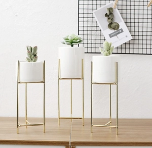 Dettaglio di supporti per piante in metallo dorato con tre vasi in ceramica bianca chic