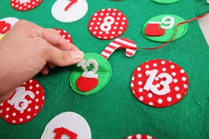 Macro view of hand opening pocket number twelve on green felt Christmas countdown calendar