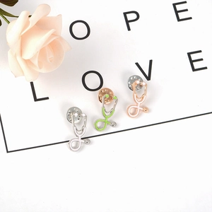 Three creative stethoscope brooches in silver, gold, and rose gold on a decorative card
