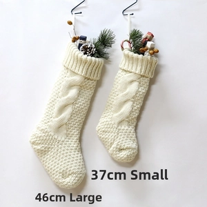 Close-up of cream cable knit Christmas stockings with pine branches and berry decor