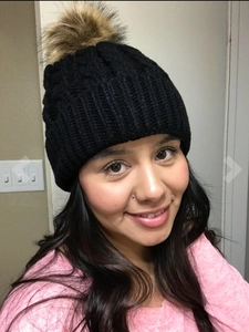 Close-up of black cable-knit beanie featuring a fluffy faux fur pompom for winter warmth