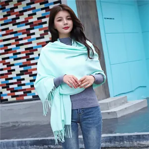 Detail of light green cashmere-feel scarf with elegant fringes on modern blue background