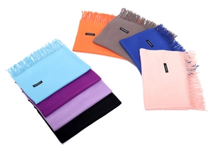 Detailed macro view showing eight solid cashmere-like scarves with long fringe and labels