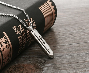 Detail of silver bullet pendant necklace with cross engraving on vintage book