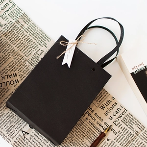 Minimalist black paper gift bag with rivet handles and a Thank You tag on a vintage desk