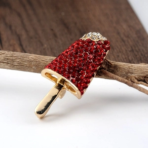 Detailed view of an ice lolly brooch with red and white rhinestones on a wooden branch