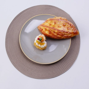 Top view of a round brown woven placemat with a houndstooth ceramic plate and gold rim