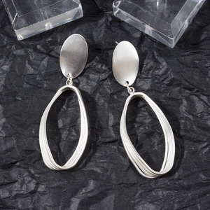 Detail of silver matte oval earrings with geometric layered hoop design on black background