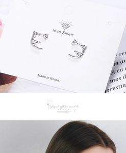 Detail of silver hollow cat head earrings shown on packaging card and model ear
