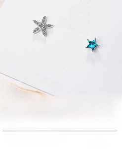 Close-up of asymmetrical blue star stud earrings with zirconia stones on white card