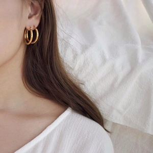 Close-up of elegant minimalist gold hoop earrings worn by a model on a soft white background