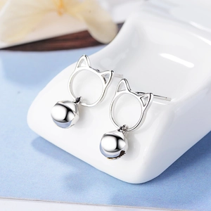 Silver hollow cat ear stud earrings with bell pendant on white ceramic stand