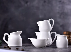 Macro view of white ceramic mini milk pitchers with ergonomic handles and pour spouts