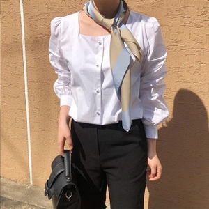 Detail showing a cream and blue heart pattern silk scarf tied on a white puff sleeve shirt