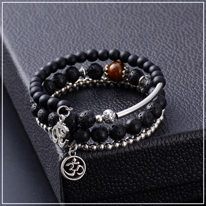 Macro detail of multi-layer lava stone bracelet with Om metal charms on black leather
