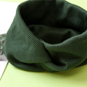 Close-up of dark green knitted headband featuring a cross-knot and ribbed texture detail