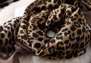 Detailed close-up of leopard print silk scarf with satin sheen on white plush surface