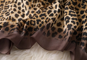 Detailed macro view of leopard print silk scarf with gradient brown edges on plush background