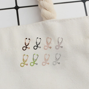 Multiple colorful stethoscope alloy brooches neatly arranged on a beige canvas bag