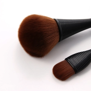 Detail of two makeup brushes with dark brown synthetic bristles and textured black handles