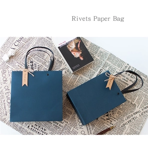 Detail of blue paper gift bag with rivet handles, thank you tag and flat lay props